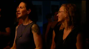 Two women smile and watch an event in the dark.