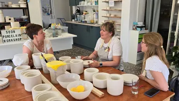 Drei Frauen sitzen an einem Tisch voller Porzellangegenstände.