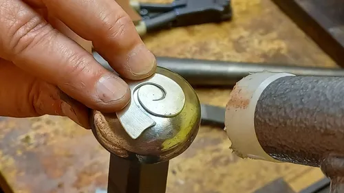 A hand forms a metallic object on a workbench.