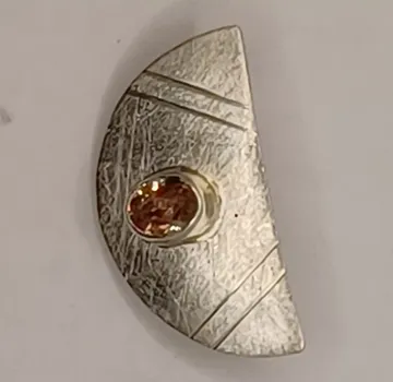 Silberner Schmuck mit einem orangefarbenen Stein, geometrisch gestaltet.