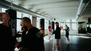 Trainer lächelt, während Teilnehmer im Fitnessstudio trainieren.