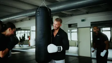 Black punching bag swings while people work out at the gym
