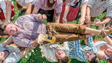 Man is held by friends, beer splashes, happy party.