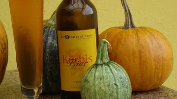 A bottle of pumpkin beer is on the table next to pumpkins.