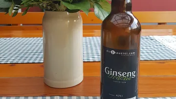Bottle of ginseng dragon stands next to vase on table.