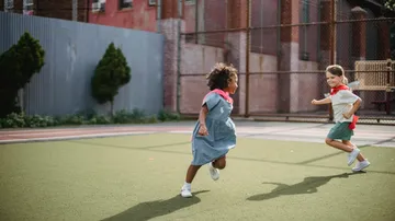 Zwei Kinder rennen spielend auf einem Sportplatz.