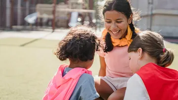 Three kids laugh as they play on a playground.