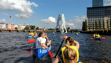 Canoeists paddle on a waterway with a sculpture.