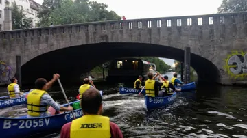 People paddle in canoes under a bridge in Berlin.