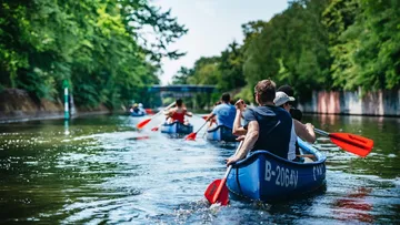 Canoes paddle on a calm, wooded body of water.