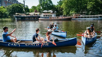 Two groups of people paddle in blue canoes on a lake.