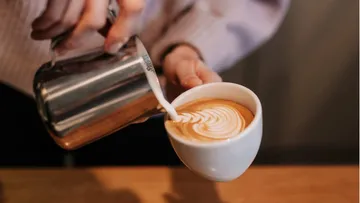 Eine Kaffeetasse wird mit Milch gegossen, um Kunst zu schaffen.