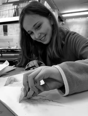 Girl smiles, erases sketch in an art space.