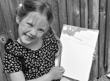 A girl is smiling, holding a sketchbook and pen.