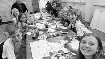Children paint at a long table in the studio.
