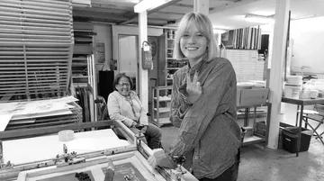 Young woman points at a printing press in a studio.