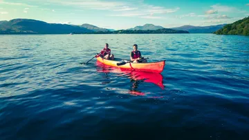 Zwei Personen sitzen im Kajak, paddeln auf einem See.