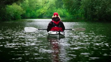 A kayaker calmly paddles on a green body of water.