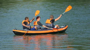 Drei Personen paddeln in einem orangefarbenen Kajak auf Wasser.