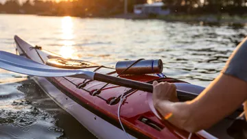 Kajak auf dem Wasser, paddelnd bei Sonnenuntergang.