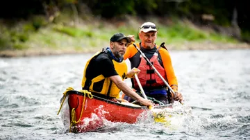 Zwei Männer paddeln in einem roten Kanu auf Wasser.