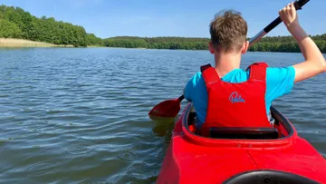 Junger Mann paddelt in rotem Kajak auf ruhigem See.