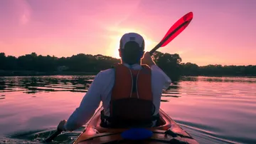 Paddler im Kajak bewegt sich ruhig, Sonnenuntergang leuchtet.