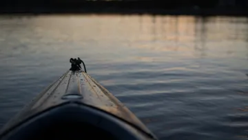 Kajak schwimmt ruhig auf spiegelndem Wasser bei Sonnenuntergang.