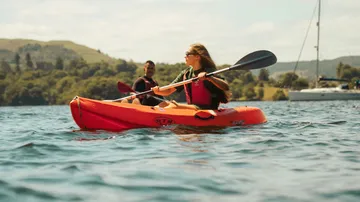 Rotes Kajak fährt auf Wasser mit zwei Personen.