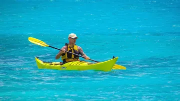 Kajakfahrer paddelt auf klarem, blauem Wasser.