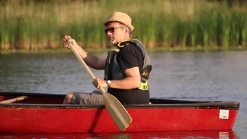 Man paddles in a red canoe on calm water.