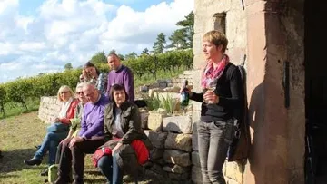Group sits at the vineyard while woman presents drinks.