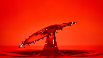 A drop of water splashes up against a red background.