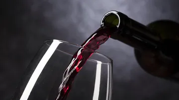 A bottle pours red wine into a wine glass.