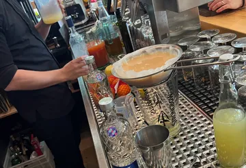 Bartender films cocktails and filters liquid at the counter.