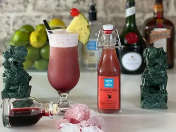 Cocktailglas mit Getränk, umgeben von Flasche und Deko.
