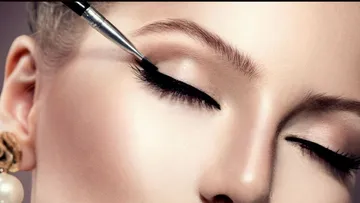 Woman receives close-up eye makeup with brush.