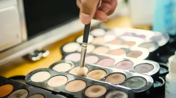 Pinsel hebt Lidschattenfarbe von Schminkpalette auf einem Tisch.