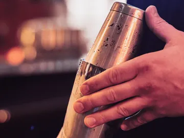 Ein Shaker wird von einer Hand gehalten, im Hintergrund verschwommen.