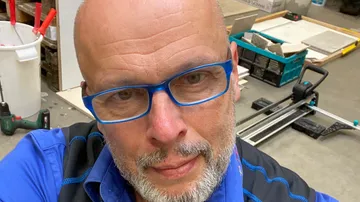 Baldmann schaut in die Kamera, umgeben von Werkzeugen.