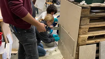 Personen verlegen Platten in einem Werkstattumfeld mit Materialien.