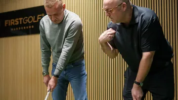 Zwei Männer üben Golfputting in einer Indoor-Anlage.