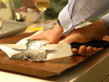 Fisch wird auf einem Holzbrett mit einem Messer Filetiert.