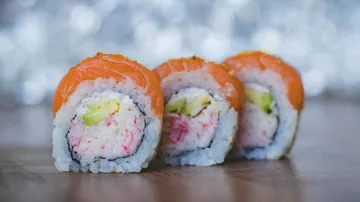 Drei Sushi-Rollen liegen auf einem Holzbrett.