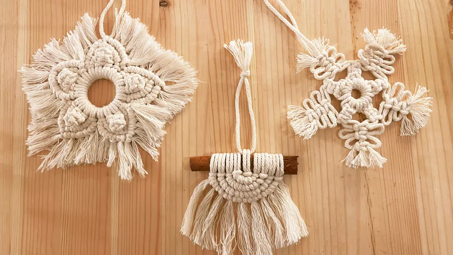Three white macrame decorations hang from wood