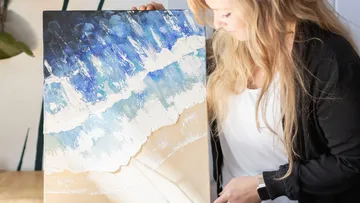 Woman holding a Fuerdende beach painting and looks at it attentively.