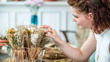 Woman arranges dried flowers in a basket.