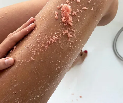 Hand applying pink body scrub on leg.