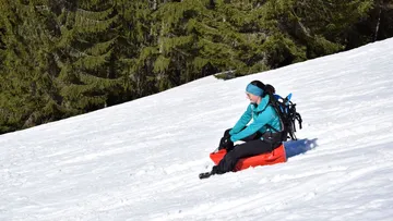 A woman is sitting on a red sled in the snow.