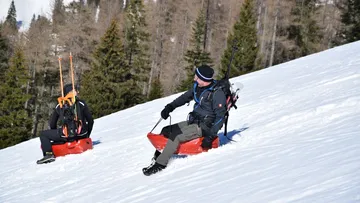 Zwei Personen sitzen auf roten Schlitten im Schnee.